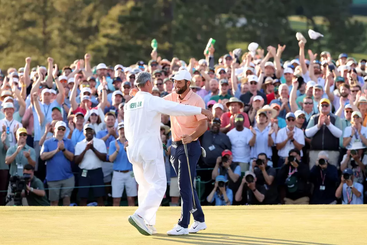 Scottie Scheffler and caddie Ted Scott celebrate on the 18th green after winning the 2024 Masters Tournament at Augusta National Golf Club 