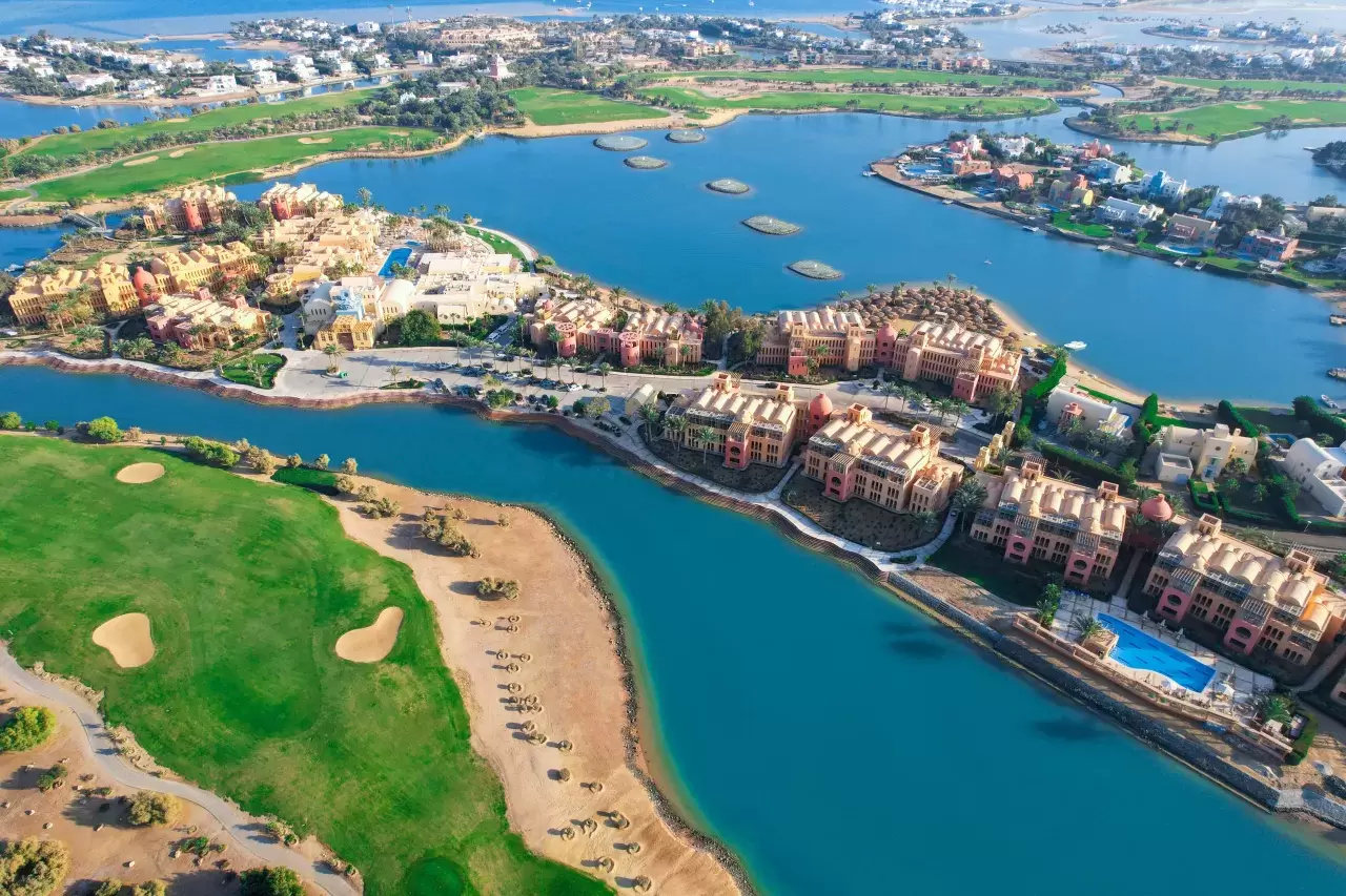 Golf hat in Ägypten eine lange Tradition. 1889 wurde der älteste Golfclub Afrikas eröffnet. Genau 100 Jahre später hat der ägyptische Milliardär Samih Sawiris mit dem Bau seines Vorzeigeresorts begonnen, nachdem er eigentlich nur den schönsten Ort am Roten Meer gesucht hatte, um für sich ein Haus und einen kleinen Bootsanlegeplatz zu bauen. Inmitten einer künstlich angelegten Lagunenlandschaft wurde daraus eine ganze Kleinstadt und ein Ferienresort mit 18 Hotels und über hundert Restaurants, Bars und Clubs